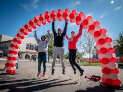 Three alumni jumping up under balloon arch